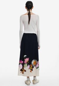 Lange zwarte rok met bloemenprint met rozen, witte en gele bloemen aan de onderrand, gecombineerd met een aansluitend wit langärmelige top.