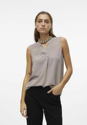 Blouse sans manches gris clair avec un décolleté en V, en tissu texturé et à coupe drapée, associée à un pantalon noir et un collier en perles argentées.