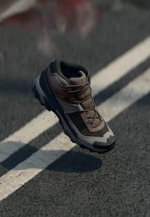 Brown and gray hiking shoe with a textured surface, padded collar, and a rugged sole. Features laces and branding on the side.
