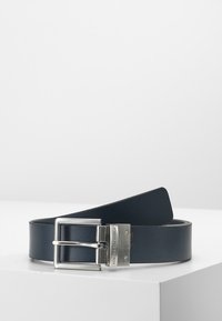 Cintura in pelle blu marino con una texture liscia, dotata di una fibbia in metallo argentato e di una fascia rettangolare che si assottiglia verso un'estremità.