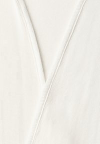 Close-up af blødt hvidt ribbet stof med en V-formet halsudskæringsøm, der fremhæver tekstur og syningsdetaljer.