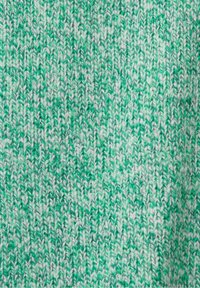 Gros plan sur un tissu tricoté vert et blanc avec une texture côtelée régulière montrant des brins de fil entrelacés.