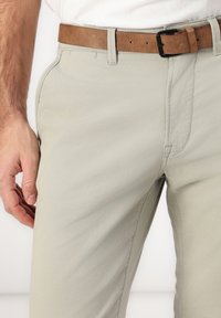 Pantaloni di cotone beige chiaro con una texture liscia, tasche laterali e una cintura in pelle marrone con fibbia nera.