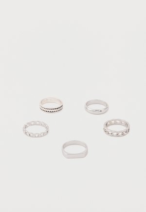 Öt ezüst gyűrű különböző mintákkal, többek között láncszemekkel, sima pántokkal és geometriai alakzatokkal, fehér felületen elrendezve.