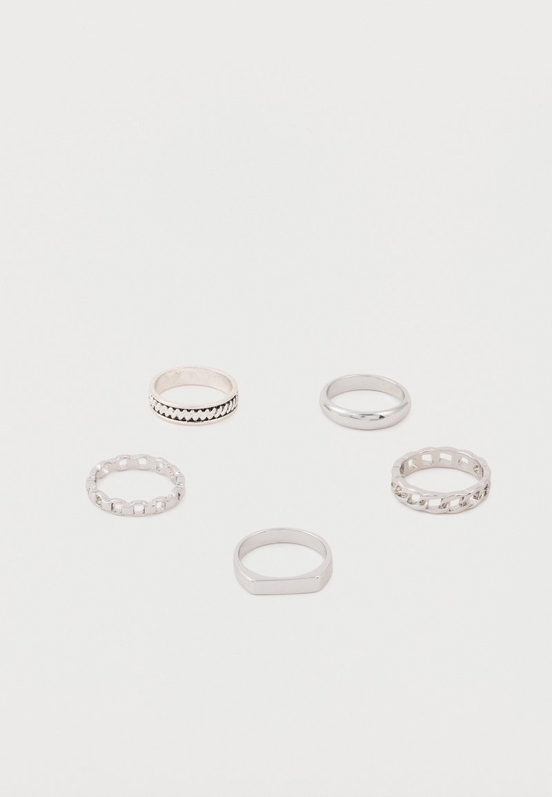 Πέντε ασημένια δαχτυλίδια με διαφορετικά σχέδια, όπως αλυσίδες, λείες μπάντες και γεωμετρικά σχήματα, τοποθετημένα σε λευκή επιφάνεια.
