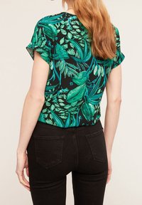 Top a manica corta con un motivo di foglie tropicali in tonalità di verde su uno sfondo nero, abbinato a jeans neri aderenti.