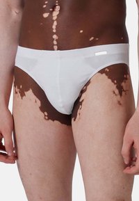 Caleçons en coton blanc avec un design sans couture, présentant une taille lisse et des motifs de pigmentation cutanée contrastants sur les cuisses.