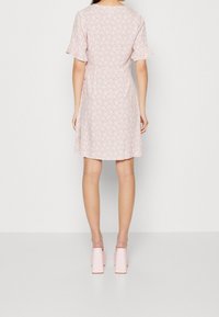 Short pink dress with a floral pattern, flutter sleeves, fitted waist, and a flowy skirt. Worn with light pink block-heeled shoes.