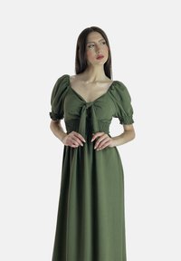 Robe maxi verte avec des manches bouffantes et un détail de nœud à l'avant. Corsage smocké, jupe fluide, fabriquée en tissu léger.