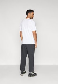 Camiseta blanca de manga corta combinada con pantalones deportivos gris oscuro y zapatillas negras con detalles verdes, vista desde atrás.