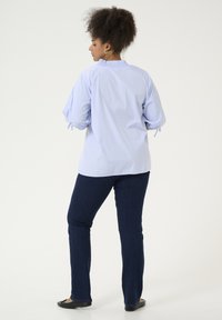 Blusa de rayas azul claro con mangas abullonadas y detalles de lazo, combinada con pantalones de mezclilla azul oscuro. Textura suave y corte relajado.