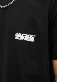 Schwarzes Baumwoll-T-Shirt mit einem strukturierten weißen Logo "JACK & JONES" im linken Brustbereich. Hat einen runden Halsausschnitt und kurze Ärmel.