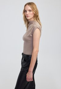 Jasnonutowy, dopasowany top z podwyższonym kołnierzem i krótkimi rękawami, w połączeniu z wysokogatunkowymi czarnymi skórzanymi spodniami. Gładka tekstura, minimalistyczny design.