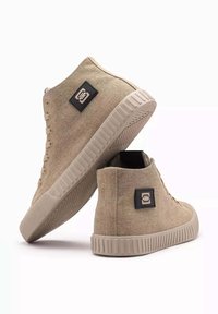 Zapatillas altas de color beige hechas de tejido texturizado, con suela de goma, sistema de lazada con ojetes y un parche con el logo en el lateral.