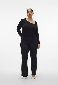 Μαύρο μακρυμάνικο τοπ με ασύμμετρο ντεκολτέ, συνδυασμένο με μαύρο παντελόνι καμπάνα και μπεζ παπούτσια με τακούνι. Απλός και μονοχρωματικός σχεδιασμός.