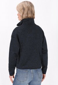 Tumed sinise värvi fleecemantel, millel on tekstuuriga heather finish. Omab kõrget krae ja pikki varrukaid, koos teksapükstega.