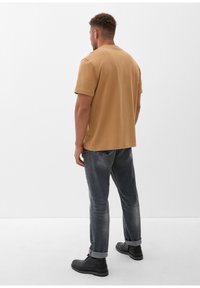 Bruine katoenen t-shirt met korte mouwen, gecombineerd met grijze spijkerbroeken. Zwarte enkellaarsjes maken de outfit compleet. Eenvoudig ontwerp, geen patronen.