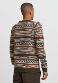 Pulover cu model marron, având modele geometrice roșii și crem, cu manșete și tiv cu reazăm. Textură tricotată cu guler rotund.