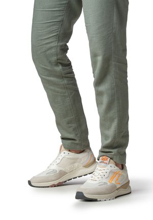 Weiße Turnschuhe mit orangefarbenen Akzenten und einer beigen Wildlederkappe. Strukturierte Stoffhose in Olivgrün. Flache Sohle und Schnürdesign.