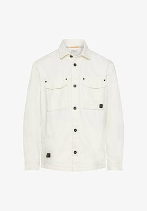 Weiße Jeansjacke mit Knopfleiste, zwei aufgesetzten Brusttaschen mit Klappen, schwarzen Knöpfen und einem kleinen schwarzen Logoaufnäher am vorderen Saum.