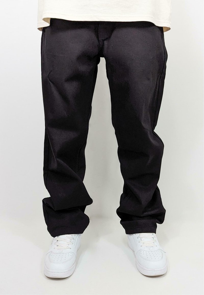 Svarte bukser laget av solid stoff med rett ben-design, kombinert med hvite joggesko. Ingen synlige mønstre eller dekorasjoner.
