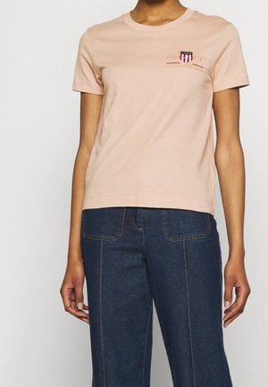 Personne portant un t-shirt rose clair à manches courtes avec un petit logo sur la poitrine et un jean taille haute bleu foncé avec poches avant et détails de couture.