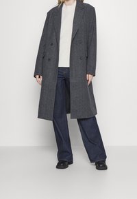 Grijze wolmix dubbelzijdige jas met een lange silhouet, gecombineerd met een lichte trui en wijde donkere jeans. Glad textuur, minimalistische details.