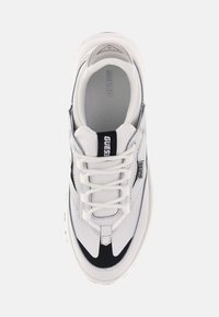Sneaker bianca con accenti neri, dotata di una tomaia texturizzata, punta arrotondata e lacci prominenti. Marchio visibile sul lato e sulla linguetta.
