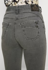 Grå denimjeans med en tajt design, två bakfickor med böjd sömnad och en läderlogotapp vid midjan.