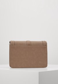 Brązowa torebka kopertowa z sztucznej skóry o gładkiej fakturze, prostokątnym kształcie i przeszyciach wzdłuż górnej krawędzi. Szczegół z magnetycznym zapięciem.