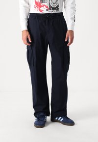 Marina cargobyxor med elastisk midja och dragsnöre. Har två stora sidofickor och en avslappnad passform. Kommer med blå sneakers.