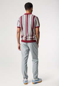 Polo de punto para hombres con un patrón texturizado en crema, rojo y azul marino, combinado con pantalones grises claros y zapatillas con patrón.