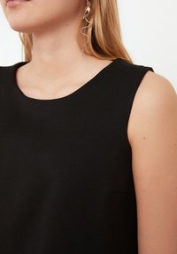Černý bezrukávový top s oblé linii výstřihu. Hladká tkanina s jemným leskem a malou, šikmou kapsou na boku. Jednoduchý a elegantní design.