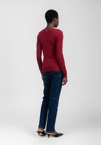 Maglietta rossa a maniche lunghe con scollatura rotonda e orlo a costine, abbinata a jeans dritti blu scuro e mule con tacco neri.