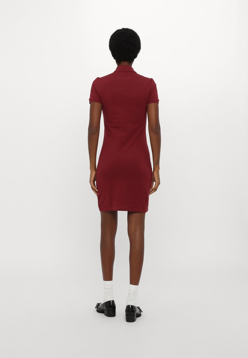 Robe polo bordeaux à manches courtes, design ajusté et col. Texture de tissu lisse, longueur genou, associée à des chaussures noires et des chaussettes blanches.