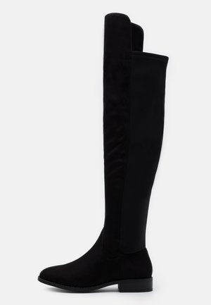 Botte plate noire montant au-dessus du genou avec bout arrondi, talon bas et dessus lisse contrastant avec un panneau arrière à texture semblable au daim.