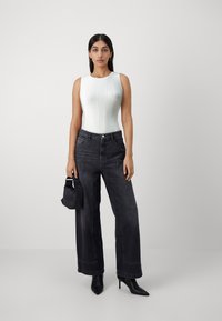 White ribbed sleeveless bodysuit paired with high-waisted black wide-leg jeans, black heeled boots, and a small black handbag.