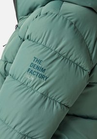 Zielona pikowana kurtka puchowa o gładkiej teksturze. Posiada wszyte panele oraz haftowane logo "THE DENIM FACTORY" w ciemnoniebieskim kolorze.