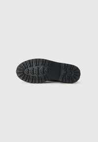 Black rubber boot sole with deep, rugged tread pattern designed for traction, shown against a plain light gray background.