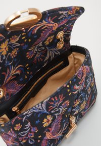 Fekete szövet táska színes virágos hímzéssel, aranyszínű fém kiegészítőkkel és mágneses patent zárással. A belső rész cipzáras zsebbel és bézs béléssel rendelkezik.