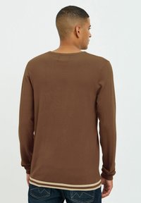 C�ămașă maro cu mânecă lungă, cu mansete striate și tiv în dungi, fabricată dintr-un material ușor, având un gât rotund și un design simplu.