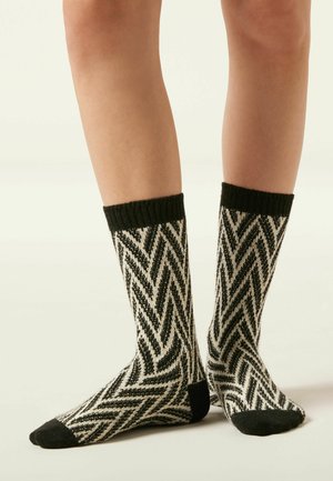 Chaussettes à motifs noir et blanc avec un design en chevron, présentant un bord côtelé noir et des accentuations de pointe noires unies. Texture douce.