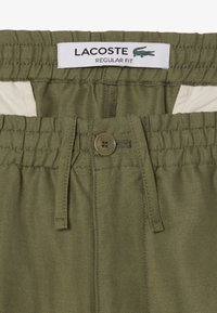 Olijfgroene shorts met een elastische tailleband, knoopsluiting en trekkoord. Voorzien van een Lacoste-logo label aan de binnenkant. Standaard pasvorm ontwerp.