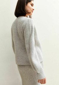 Pull en tricot gris avec texture côtelée, doté d'un col rond et de manches longues, associé à une jupe assortie, présenté de côté.