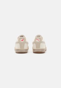 Valkoiset lenkkarit, joissa on beige mokkasiinikoristelu, teksturoitu kumipohja ja vaaleanpunainen Puma-logo kantapäässä. Klassinen matalaprofiilinen muotoilu, minimalistinen ilme.