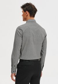 Czarna i biała wzorzysta koszula z długim rękawem, z klasycznym kołnierzykiem, slim fit i zapinanymi mankietami, noszona z czarnymi spodniami.