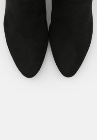 Botines de ante negro con punta afilada y textura suave, con un diseño sin cordones y tacón estructurado. Sin herrajes ni patrones visibles.