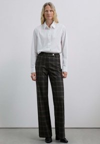 Chemise blanche à manches longues, à boutons, associée à un pantalon à carreaux taille haute de tons sombres, avec des jambes larges et un devant plat avec un détail de bouton.