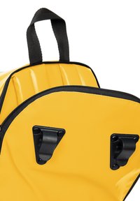 Sac à dos jaune avec une finition texturée, doté de fermetures éclair et de matériel noir, y compris deux clips noirs et une poignée supérieure pour le transport.