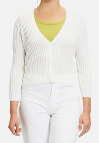 Bílý žebrovaný cardigan s výstřihem do V, s knoflíkovým zapínáním a tříčtvrtečními rukávy, přeložený přes zelený top. Textura vypadá měkce a elasticky.